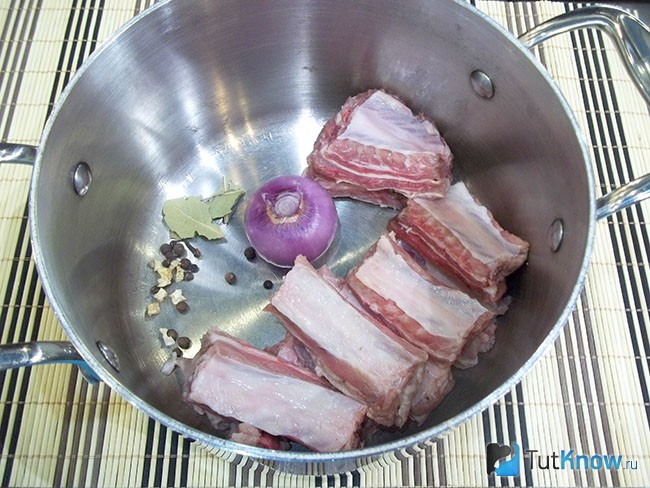 Нарезанное мясо, очищенный лук и специи лежат в кастрюле для варки бульона