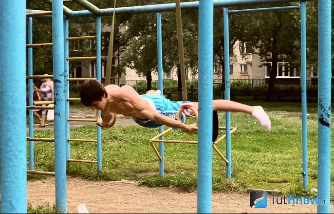 Спортсмен тренируется на кольцах на спортивной площадке