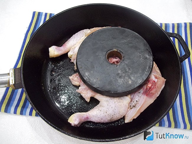 Цыпленок жарится на сковороде под грузом