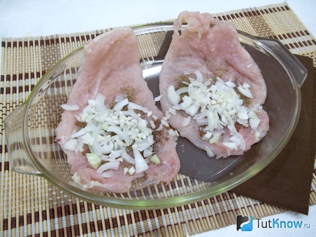 На куриное филе выложен лук и чеснок