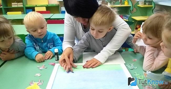 Женщина помогает деткам приклеивать куски салфеток