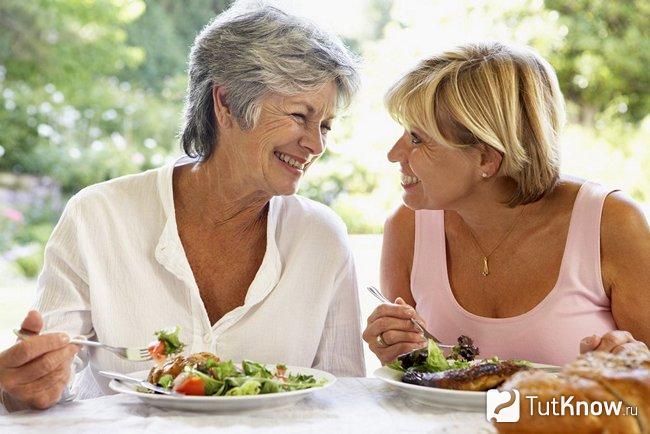 Две возрастные женщины едят на свежем воздухе