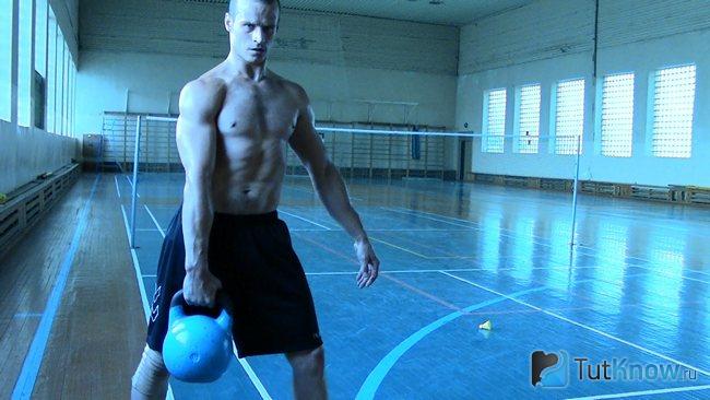 Парень тренируется при помощи гири