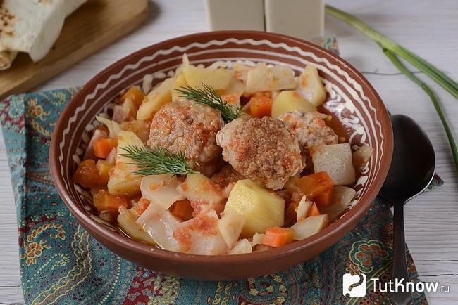 Порция готового рагу с картошкой и фрикадельками подана к столу