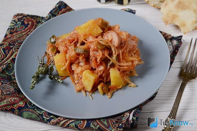 Солянка из квашеной капусты с сосисками и картошкой выложена на тарелочку