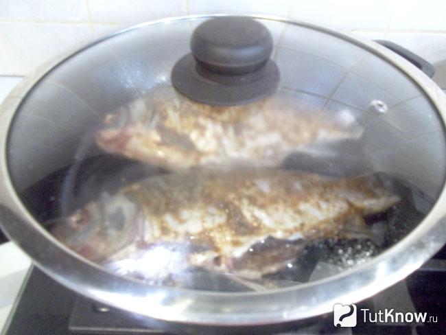 Карась жарится на сковороде в соусе под крышкой