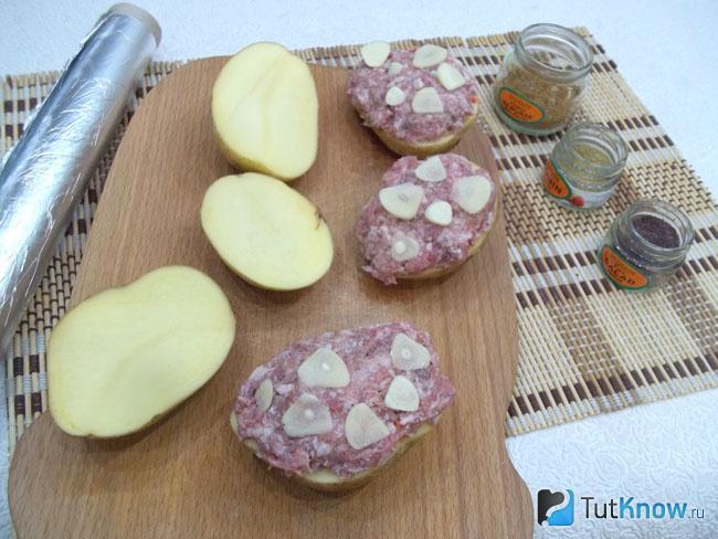 На половинку картофеля выложен фарш и ломтики чеснока