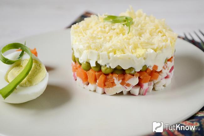 Салат из крабовых палочек с зелёным горошком и морковкой на тарелке
