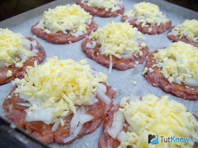Котлеты из фарша присыпаны сырной стружкой и запекаются в духовке