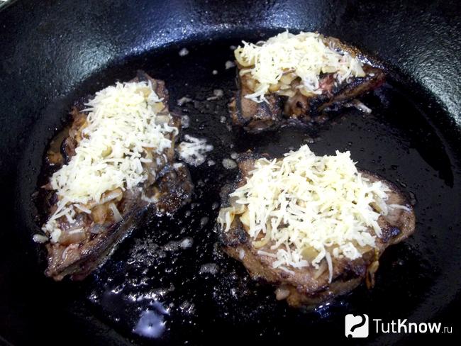Печеночные отбивные присыпаны луком и сырной стружкой
