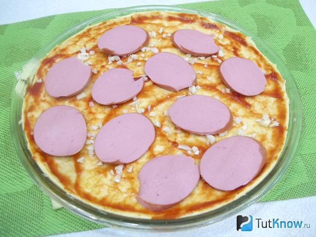 На тесто выложена колбаса нарезанная тонкими кольцами
