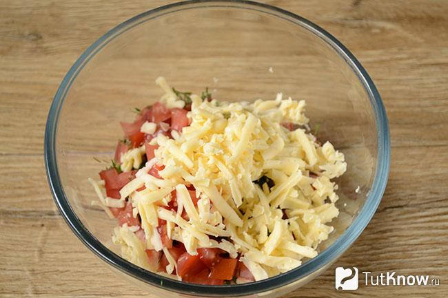 Тёртый сыр в миске с колбасками, зеленью и помидорами