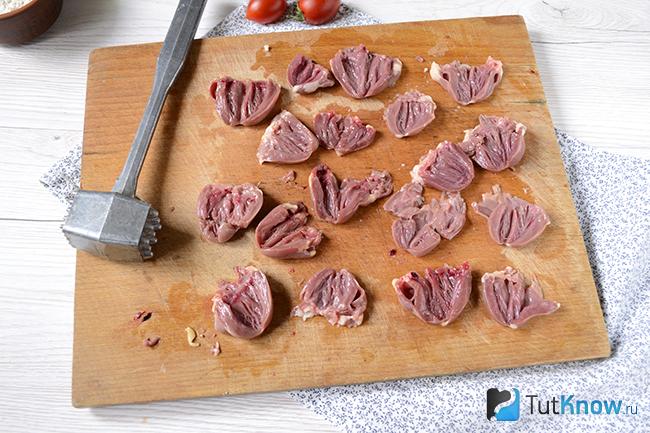 Разрезанные пополам куриные сердечки на кухонной дощечке