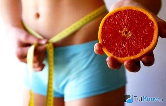 Девушка замеряет талию и держит в руке грейпфрут
