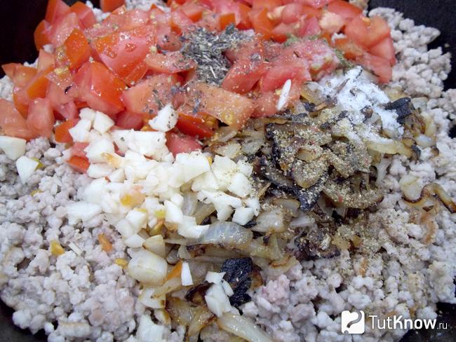 В сковороду выложены жареный мясной фарш, пассированый репчатый лук, нарезанные помидоры, соль и специи