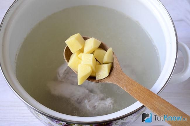 Резаная картошка над кастрюлей с бульоном