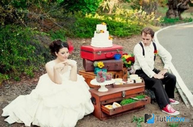 Жених и невеста сидят возле украшенных чемоданов