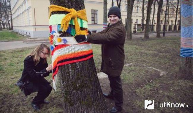 Парень и девушка украшают ствол дерева в стиле ярнбомбинг