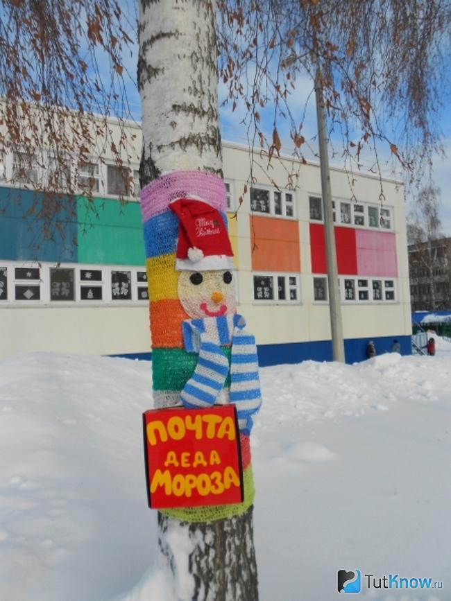 Ствол дерева украшен вязаным снеговиком