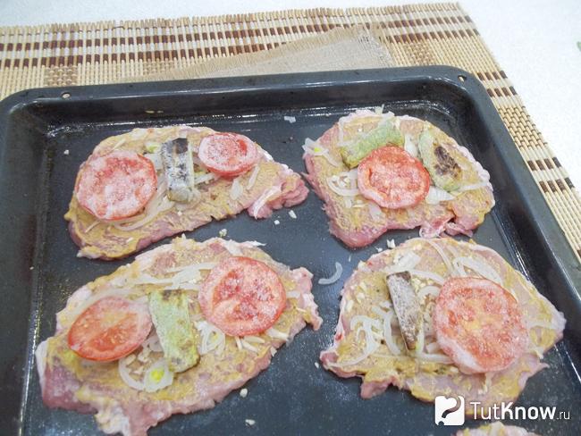 На мясо выложены кольца помидоров и кабачков