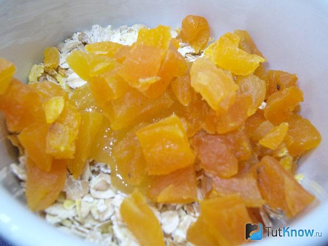 Овсяные хлопья с нарезанной курагой насыпаны в миску