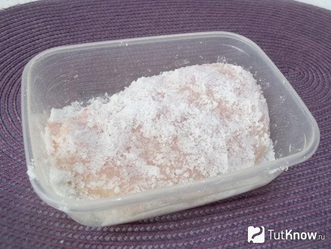 В емкость с солью опущена куриная грудка и сверху присыпана солью