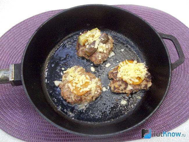 Овощи присыпаны сыром и отбивные жарятся под крышкой