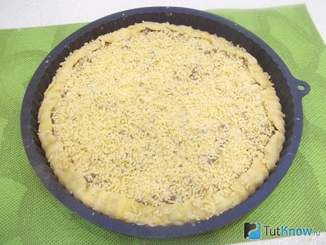 Мясной пирог из песочного теста присыпан сыром и отправлен в духовку