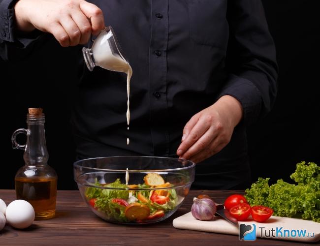 Мужчина заправляет салат соусом Цезарь