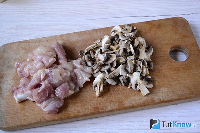 Мясо и грибы нарезаны на кухонной дощечке