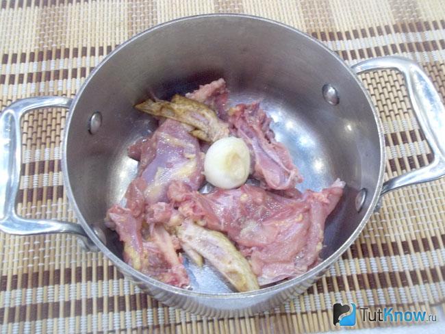 Нарезано мясо и очищенная луковица опущены в кастрюлю