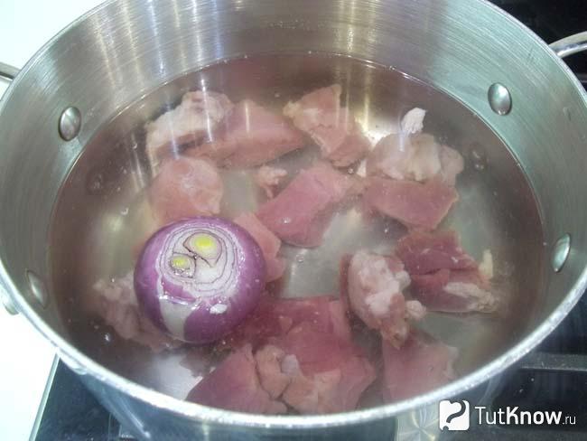Мясо с луком сложены в кастрюлю и залиты водой
