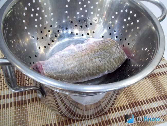 Дуршлаг с карасем установлен на кастрюлю с кипящей водой