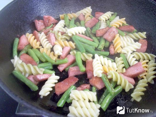 Готовые макароны с яйцами, колбасой и спаржей на сковороде